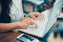 beautiful young hipster woman's hands busy working on her laptop sitting at wooden table in a coffee shop